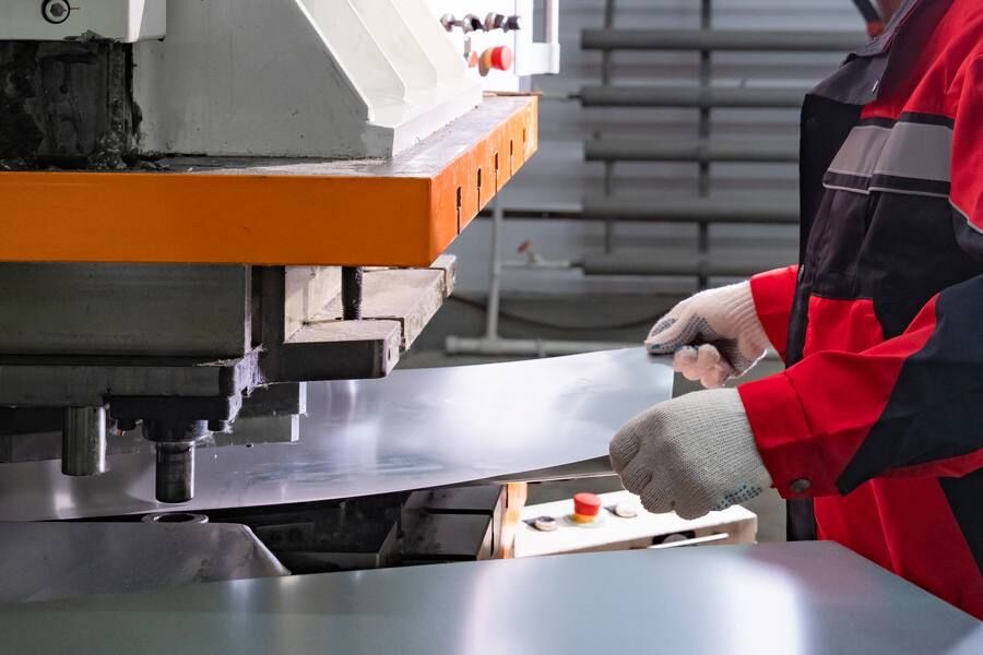 Operatore che movimenta una lamiera in acciaio su macchina di lavorazione
